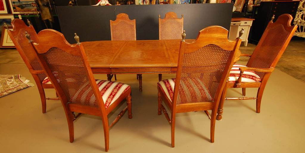 Vintage Dining Room Set: 6 wooden chairs with wicker backing and metal accents. Chairs are reupholstered. One chair is missing one post, slight scratches on wooden table surface. Burl finish on table top. 42" W 62"L.