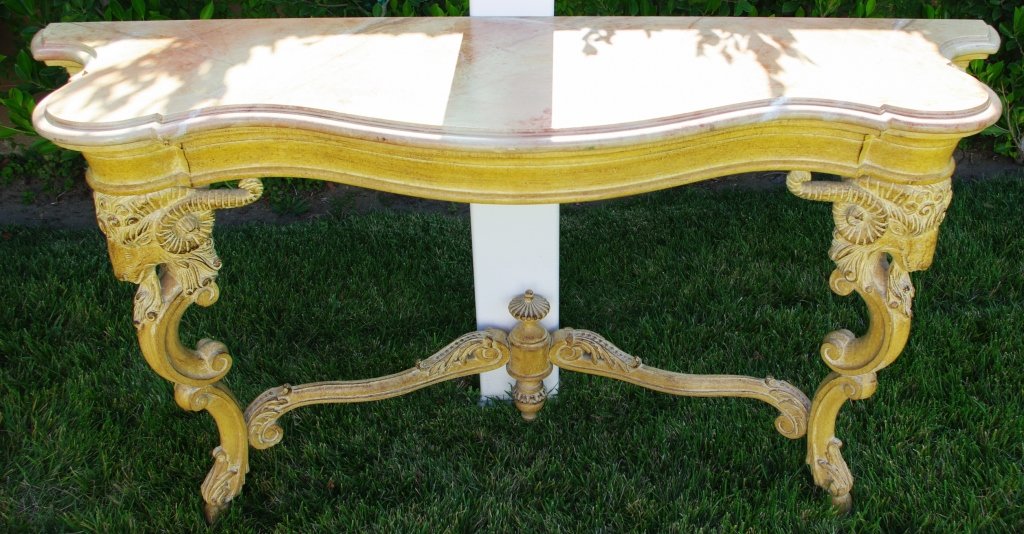 Carved Console Table, ca. Early 1930's: Rare hand carved solid wood base console table, featuring stylized rams heads and hoof design as legs, with shaped serpentine rouge faux marble top. Measures approx 31" x 57"L x 16.5" Condition: Very 