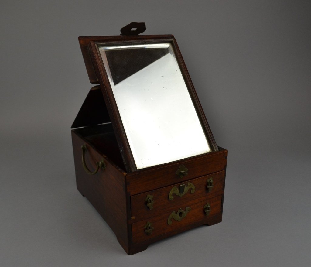 An Antique Chinese Huanghuali Mirrored Box The mirrored: The mirrored huanghuali dressing box having dual drawers with figural pulls and escutcheons, beneath the mirrored cover with figural butterfly hinges, and flanked to each side by brass handles. Size: 