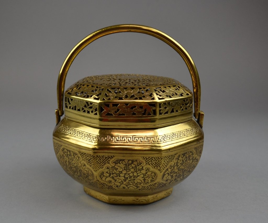 A Chinese Brass Hand Warmer Of octagonal form, the: Of octagonal form, the brass hand warmer having a Greek key upper border above the central floral medallion reserves on the interlocking fretwork ground, the whole surmounted by the pierced cover with