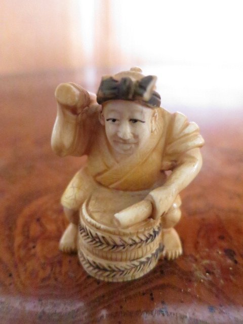 JAPANESE CARVED ANTIQUE IVORY NETSUKE, MAN & DRUM: JAPANESE HAND CARVED AND POLYCHROMED NETSUKE FIGURE OF A MAN HITTING DRUM. DIMENSIONS.2 INCHES HIGH X 1 INCHE WIDE.