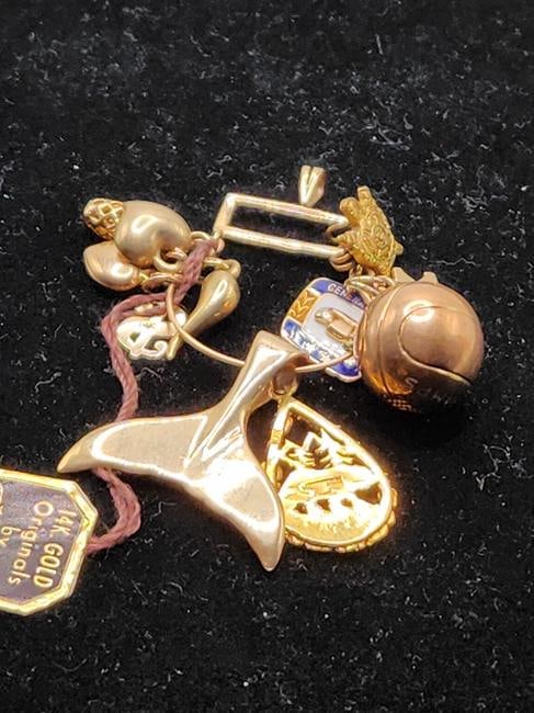 Gold Charms On Charm Holder 11 Charms: 11 Unique and Different gold charms on Charm holder. Each Charm is marked. Charm holder features a Pineapple, a crowned crest, a chili pepper, 2 gold hearts, a money sign, a whale tail, a tear drop sh