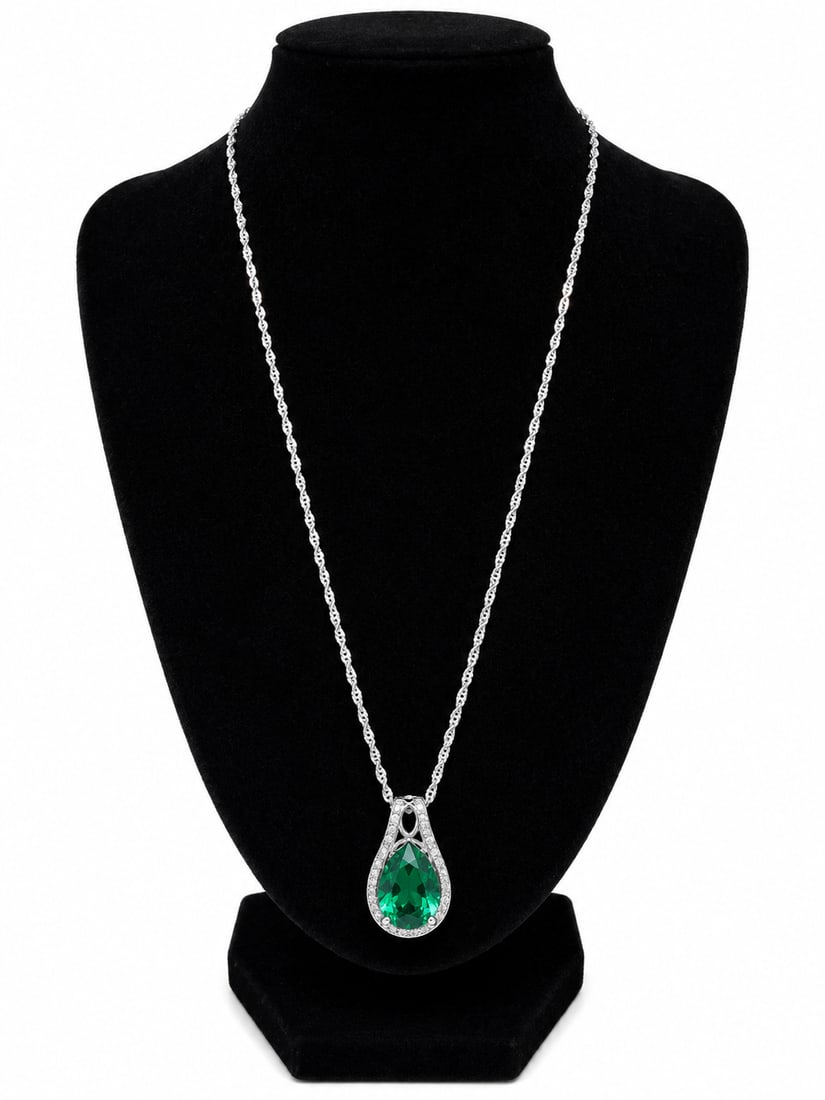 Silver Necklace with Green Teardrop Stone Pendant: Silver necklace featuring a large green teardrop shaped faceted stone pendant surrounded by clear accent stones with decorative detailing.Ships from Newport Beach, CA.