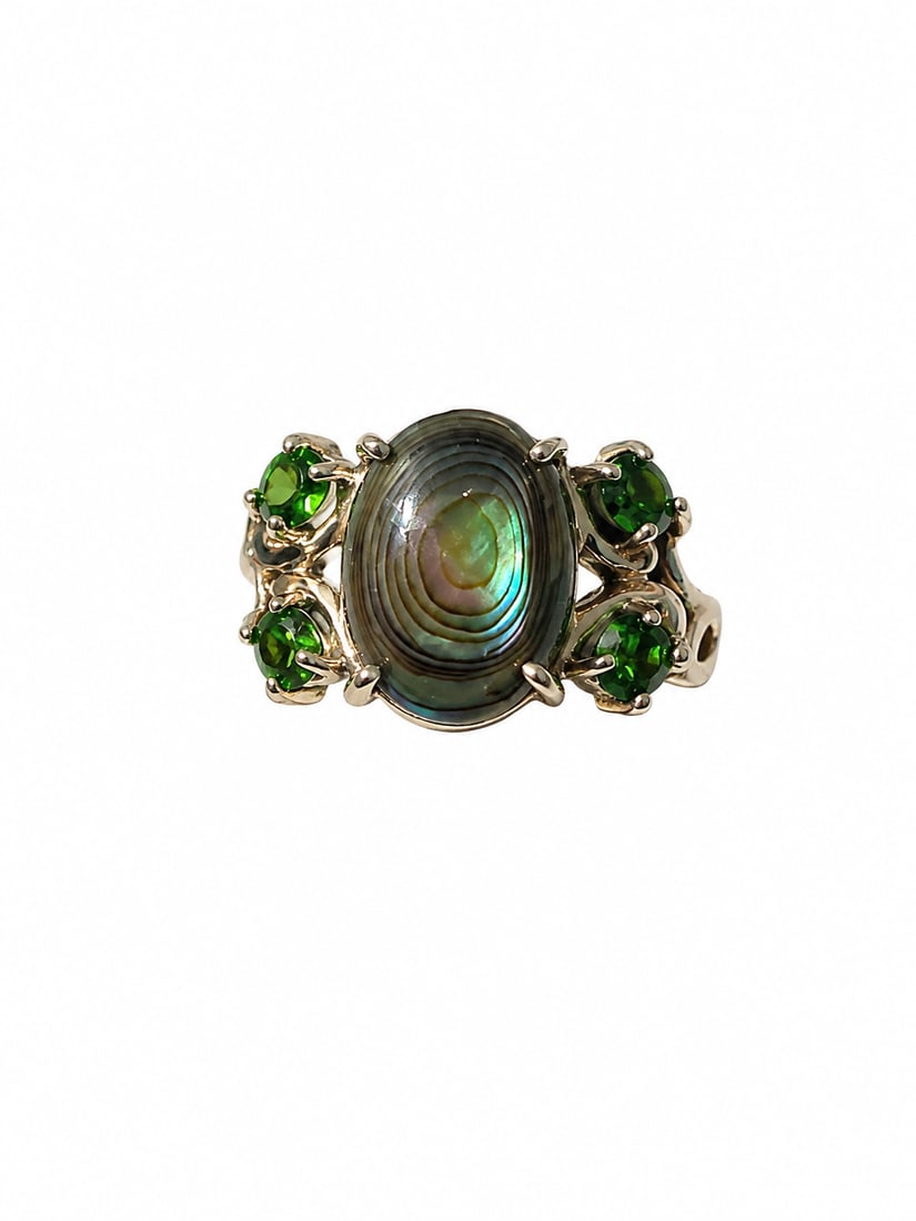 Abalone & Green Gemstone 925 Sterling Ring: Sterling silver ring featuring an oval abalone shell centerpiece with natural-looking iridescent green, blue, and bronze hues. Accented by four round faceted green gemstones in an ornate openwork
