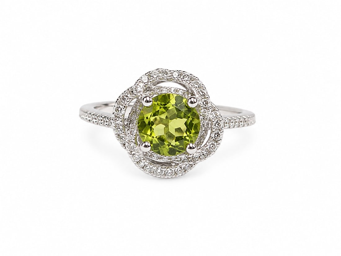 Peridot Oval Halo Sterling Silver Ring: Sterling silver ring featuring a vivid oval-cut peridot center stone surrounded by a swirling double halo of white crystal accents. Additional crystal detailing extends along the band, creating an