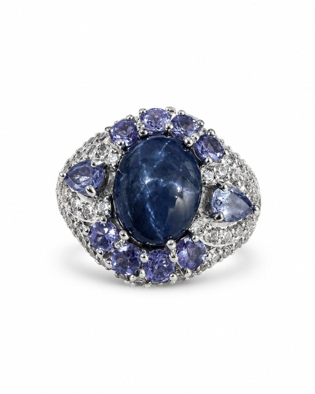Sterling Silver Blue Sapphire & Tanzanite-Like Multi-Stone Statement Ring: 925 sterling silver statement ring featuring a large oval deep-blue sapphire center stone surrounded by an ornate arrangement of violet-blue tanzanite stones and smaller clear accent stones. The wide,