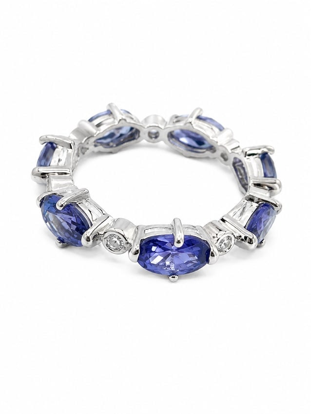 Tanzanite Oval Eternity Band Ring: Silver ring featuring a continuous arrangement of oval-cut tanzanite-colored stones accented by smaller round white crystals. The alternating settings create an elegant eternity-band design with rich 
