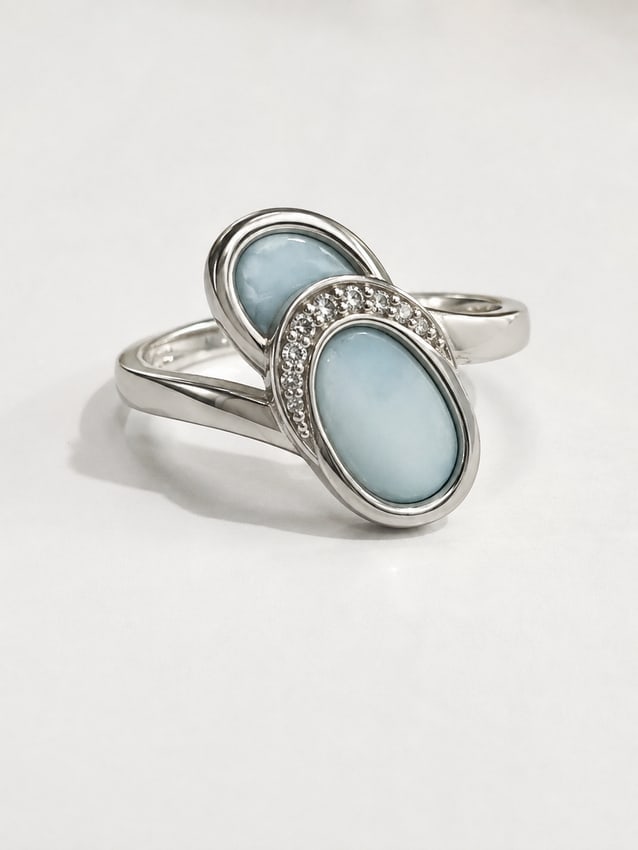 Larimar & Crystal Double Oval Sandal Silver Ring: Elegant silver ring featuring two smooth oval larimar stones in soft Caribbean blue. The overlapping design is accented with a curved row of sparkling white crystals, creating a graceful contemporary