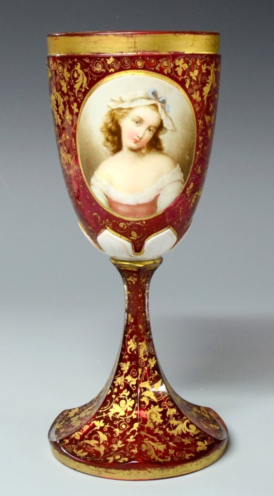 Double Overlay Glass Goblet: White over clear over cranberry. Facet-cut foot and bowl with front and rear raised white panels. Detailed enameled portrait of a woman and floral design with ornamental gilding. 8.8"ht., Bohemian, ci