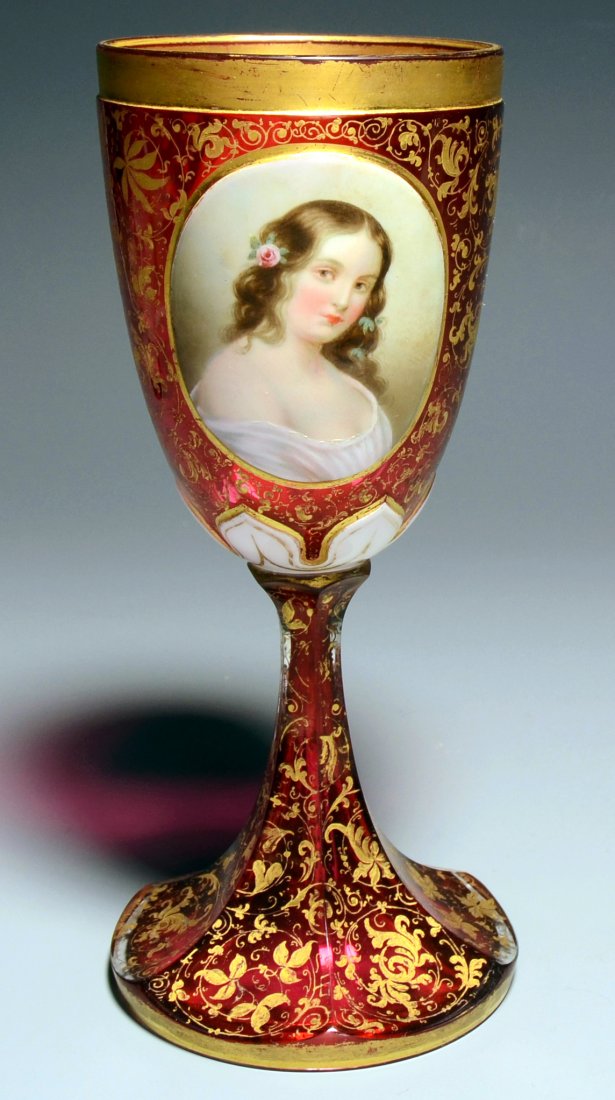 Double Overlay Glass Goblet: White over clear over cranberry. Facet-cut foot and bowl with front and rear raised white panels. Detailed enameled portrait of a woman and floral design with ornamental gilding. 8.8"ht., Bohemian, ci