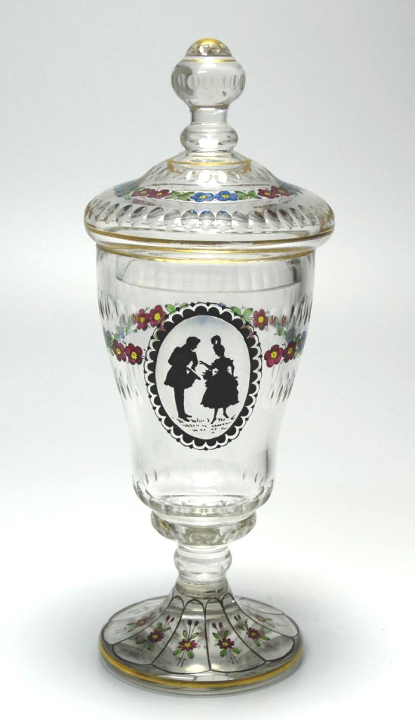 Pokal: Clear glass with circular cuts on bowl and cover, facet-cut foot. Transparent enamel floral decoration with a silhouette of a couple painted in schwarzlot. 9.8"ht., Haida, circa 1920.