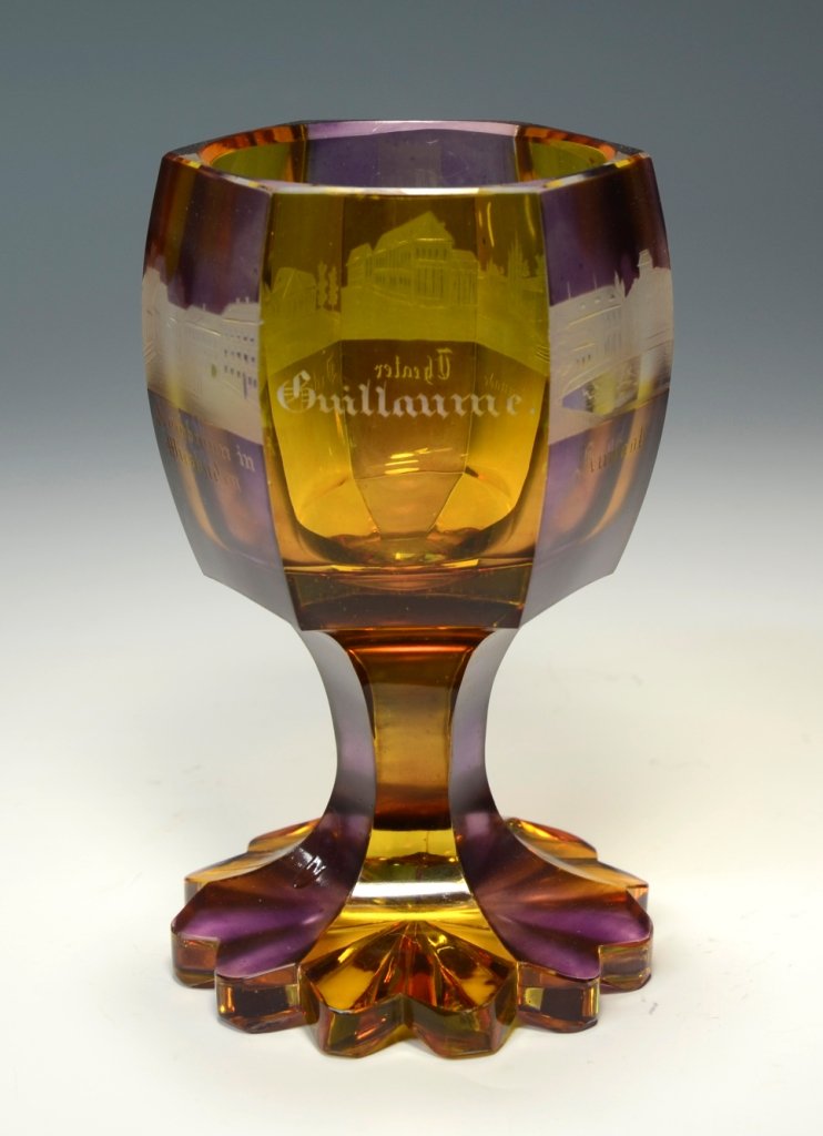 Souvenir Beaker: Blown clear glass with amber and amethyst stain. 6 facet-cuts around body, stem, and foot. Five engraved scenes. 5.0"ht., Bohemian, circa second half 1800's.