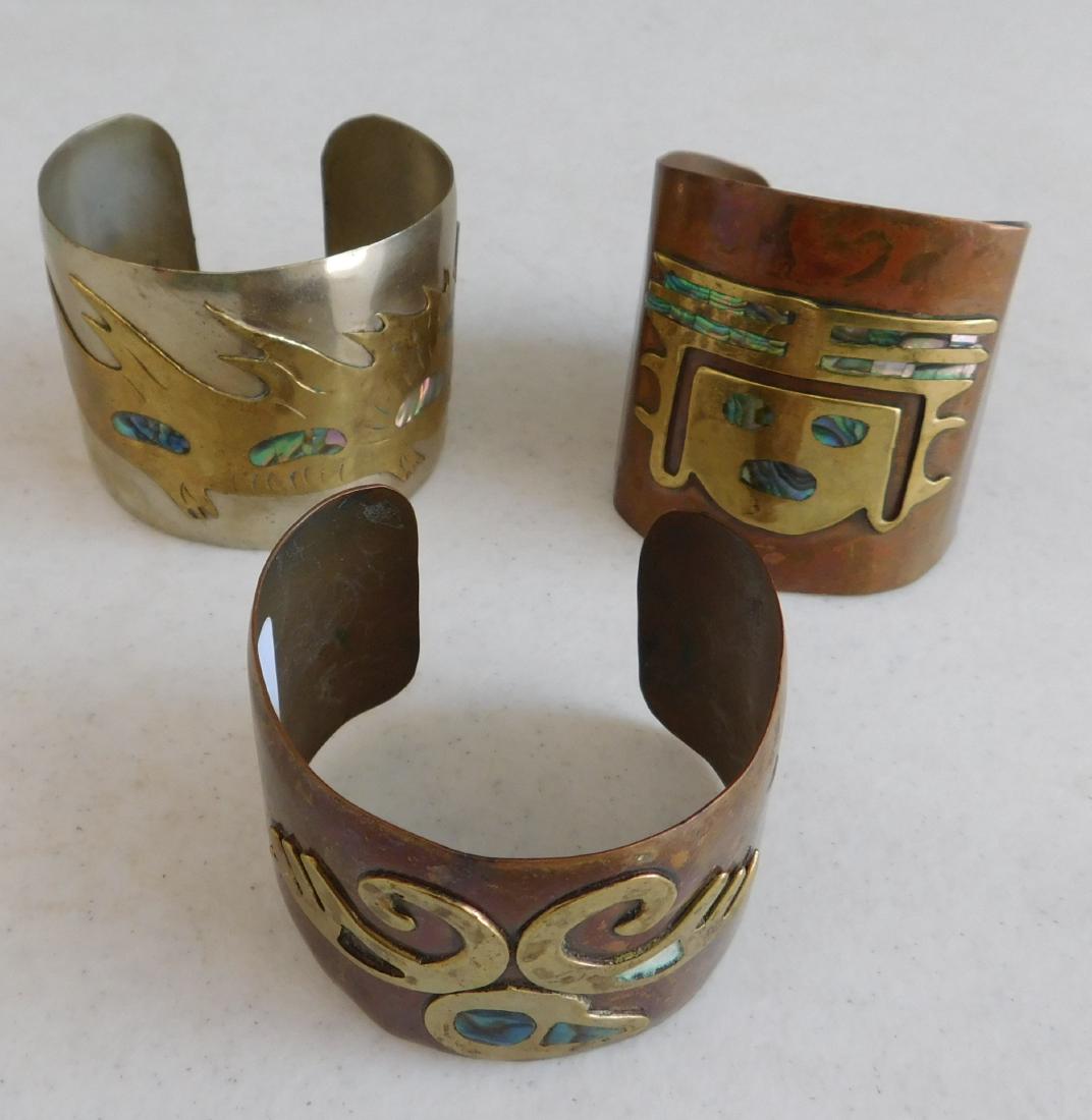 3 Mexican Mixed Metal Cuffs: 3 Mexican Mixed Metal Cuffs, circa 1940s. Made of copper, brass and abalone, the items measure 2 1/4" x 1 1/2" to 2 1/2" x 2 1/2", 7" and 6 3/4" inside measurements. Mexico. 40 grams, 57 grams, and 51