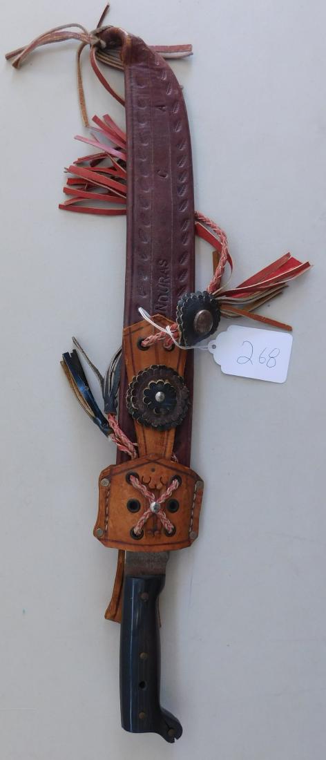 Machete & Scabbard: Machete & Scabbard, circa 1950s. Made of leather, plastic, and steel, the machete sheathed measures 25" long. Blade from Brazil, sheath from Honduras. Usable jungle knife. Condition: Very good, see im