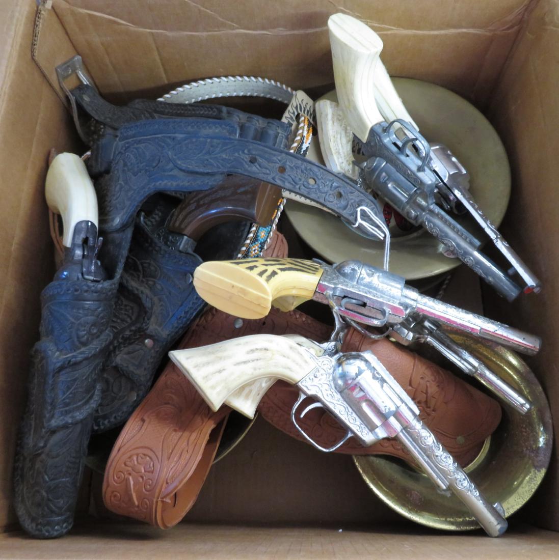 Toy Cowboy Holster + Cap Gun Collection: Toy Cowboy Holster + Cap Gun Collection, c. 1970s-80s. Made of leather, plastic, pot metal and beads, the guns measures approx. 10" in length. USA, 1 Korean spitoon. Contains 9 cap guns, 2 single hols