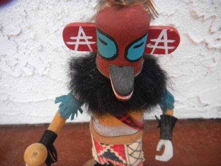 Antelope Kachina Doll: Antelope Kachina Doll signed by A John. The doll is standing on wood base and is 10 inches tall. The doll has deer hide painted skirt and fringe, leather moccasins and fringed leggings and harm bands.