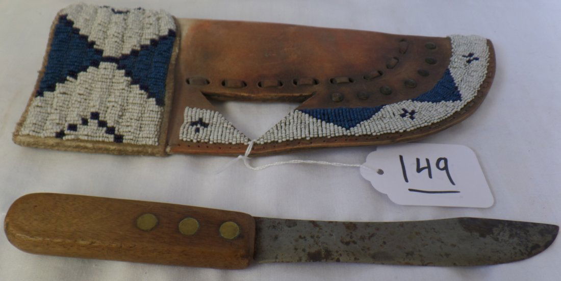 Crow Tribe Rawhide Beaded Knife Sheath & Knife: Crow Tribe Rawhide Beaded Knife Sheath & Knife circa 1940. Sheathe measures 11.5" x 4.5" and knife measures 10.5" x 1" x .5". Made of wood, steel, rawhide, glass beads and brass tacks. The knife is an
