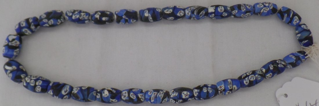 Trade Beads with Blue Faces: Early 20th Century glass, blue, white and red. Each beads has five or ten faces on it. There are minor nicks and scrapes on beads from wear. The beads measure 7/8 to 1/2 inch. The string of beads is 2