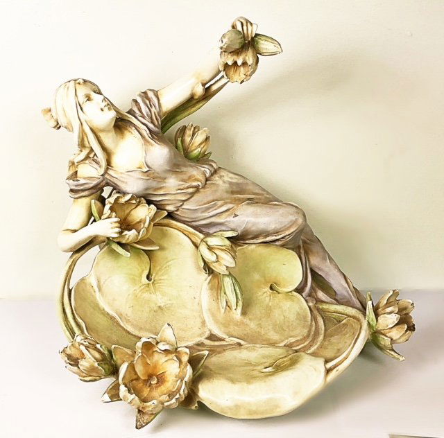 CONTINENTAL PORCELAIN GROUP OF A MAIDEN AMIDST LOTUS: Circa 1900. Marked with model # 3768 M. Possibly Amphora. The long haired beauty reclining atop clustered lotus. Height 14". Width 16". Depth 12".