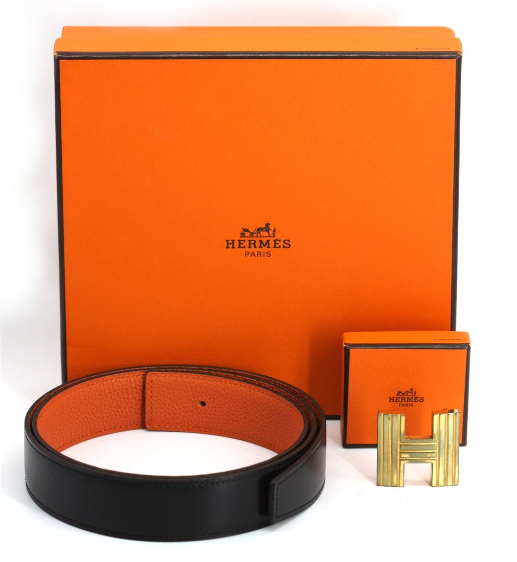 Hermès Black Leather and Gold Toned Bronze Reeded H Buckle: Hermès Black Leather and Gold Toned Bronze Reeded H Buckle The 41 inch stitched black leather strap, the reverse orange, the H buckle with textured with flutes, new, in the original fitted box. Lengt