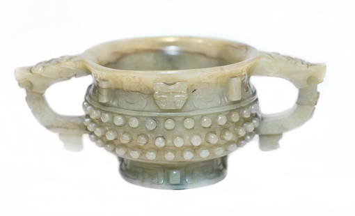 CHINESE ARCHAIC STYLE CARVED JADE TWO-HANDLED CUP: CHINESE ARCHAIC STYLE CARVED JADE TWO-HANDLED CUP Early 17th/Late 18th Century. The rounded body raised on a flared foot carved with two dragon head loop handles, the sides carved in high relief