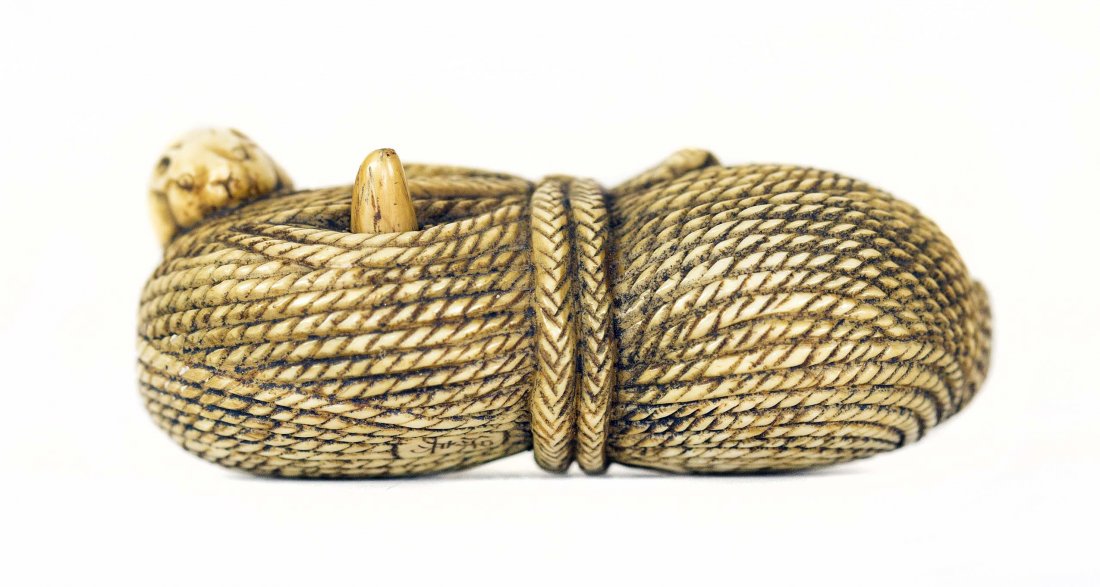 CARVED IVORY NETSUKE: PROPERTY FROM A FLORIDA COLLECTION CARVED IVORY NETSUKE Signed. Of a mouse, on a bundle of rope, crawling towards an articulated object. Length 2 1/4 inches.