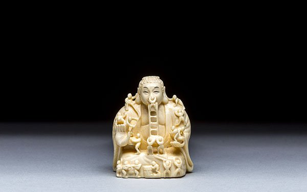 CARVED IVORY NETSUKE OF BUDDHA: CARVED IVORY NETSUKE OF BUDDHA Signed with a tiger eye plaque. Height 2 in. (5.1 cm.)