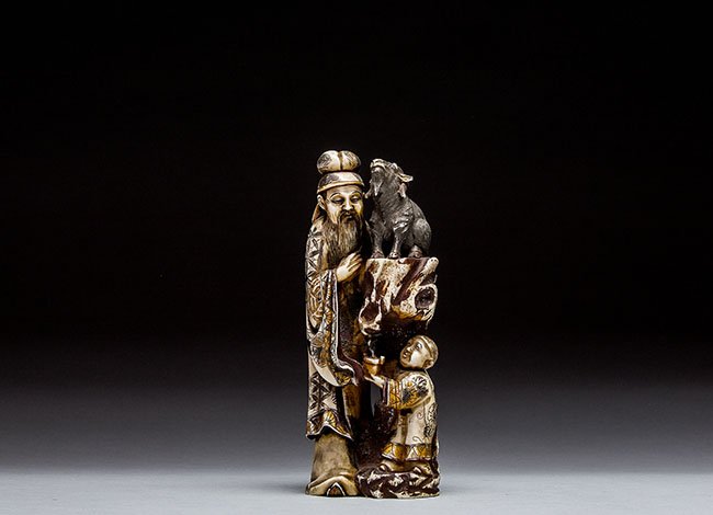 JAPANESE STLE CARVED IVORY MAN WITH BOY AND SHEEP: JAPANESE STYLE CARVED IVORY MAN WITH BOY AND SHEEP Shown standing next to a waterfall, the boy holds a cup to capture the falling water; signed with a red lacquer reserve. Height 7 in. (17.8 cm.)
