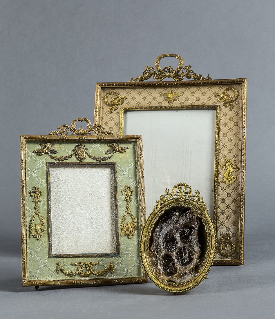 THREE OLD WORLD NEOCLASSICAL STYLE PICTURE FRAMES: THREE OLD WORLD NEOCLASSICAL STYLE GILT METAL PICTURE FRAMES Circa 1900 Two rectangular frames with a wreath and ribbon cresting, with fabric backs applied with finely cast metal trophies, wreaths, an