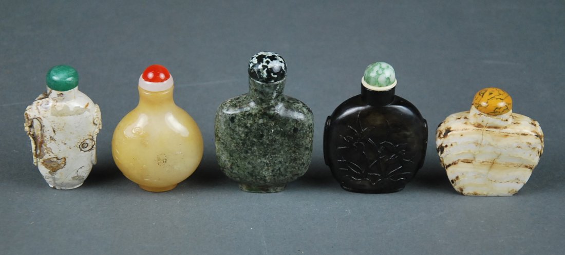 FINE CHINESE AGATE AND FOUR OTHER SNUFF BOTTLES: FIVE CHINESE ASSORTED SNUFF BOTTLES Comprising a pear shaped honey toned agate bottle carved with blossoming plum branches, circa 1880, two travertine marble examples, one with mask handles, a speckle