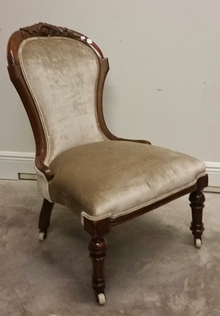 VICTORIAN WALNUT SLIPPER CHAIR, CIRCA 1870: VICTORIAN WALNUT SLIPPER CHAIR, Circa 1870, the crest carved with leaves and stylized flower, the tapered legs ending in casters. Height 34 in.