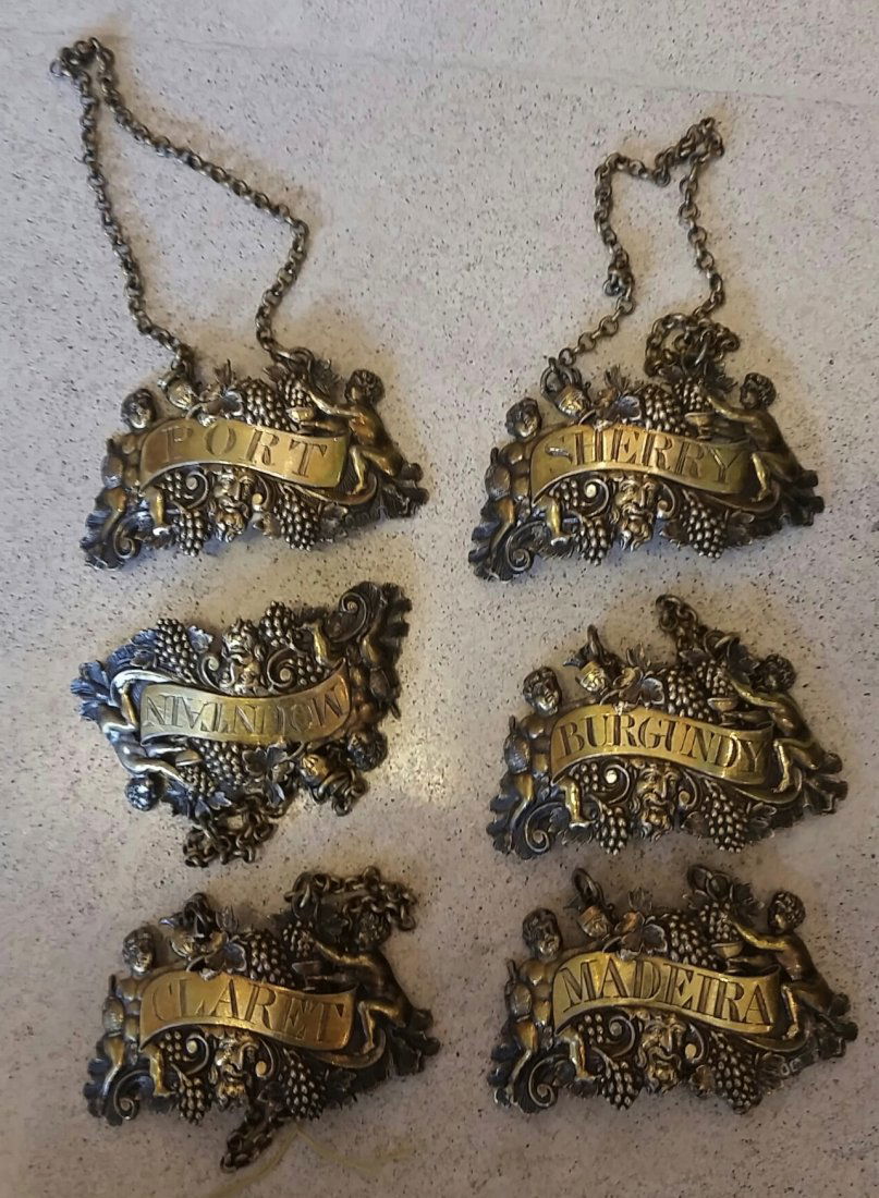 SIX VICTORIAN SILVER-GILT BOTTLE LABELS, JAMES ROBINSON: FORMERLY THE COLLECTION OF JAMES GOLDMAN, NY SET OF SIX VICTORIAN SILVER-GILT BOTTLE LABELS Mid to late 19th century, retailed through James Robinson, marked, each chased with two putti with fruit-fi