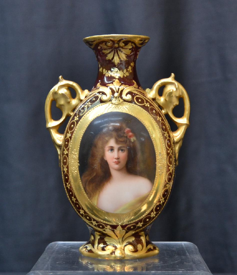 ROYAL VIENNA TWIN HANDLE PORTRAIT VASE: HAND PAINTED ROYAL VIENNA PORTRAIT VASE OF YOUNG WOMAN TITLED "CARNATION" , ARTIST SIGNED WAGNER , SURROUNDED BY HEAVY GOLD DECORATIONS OVER BURGUNDY GROUND - (HAS PROFESIONAL REPAIR AROUND NECK) 4 3/