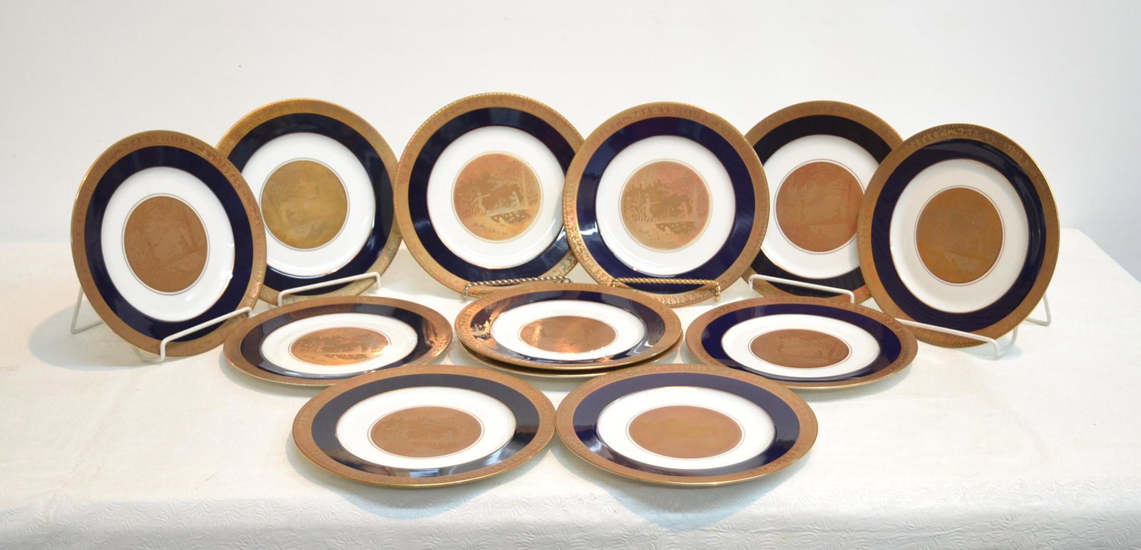 (12) ROSENTHAL COBALT & GOLD SERVICE PLATES: (12) ROSENTHAL COBALT & GOLD DECORATED DINNER PLATES WITH GOLD CENTER MEDALLION OF FIGURES IN LANDSCAPE & GOLD BORDER WITH FIGURES & CHARRIOTS - 10 1/4" D