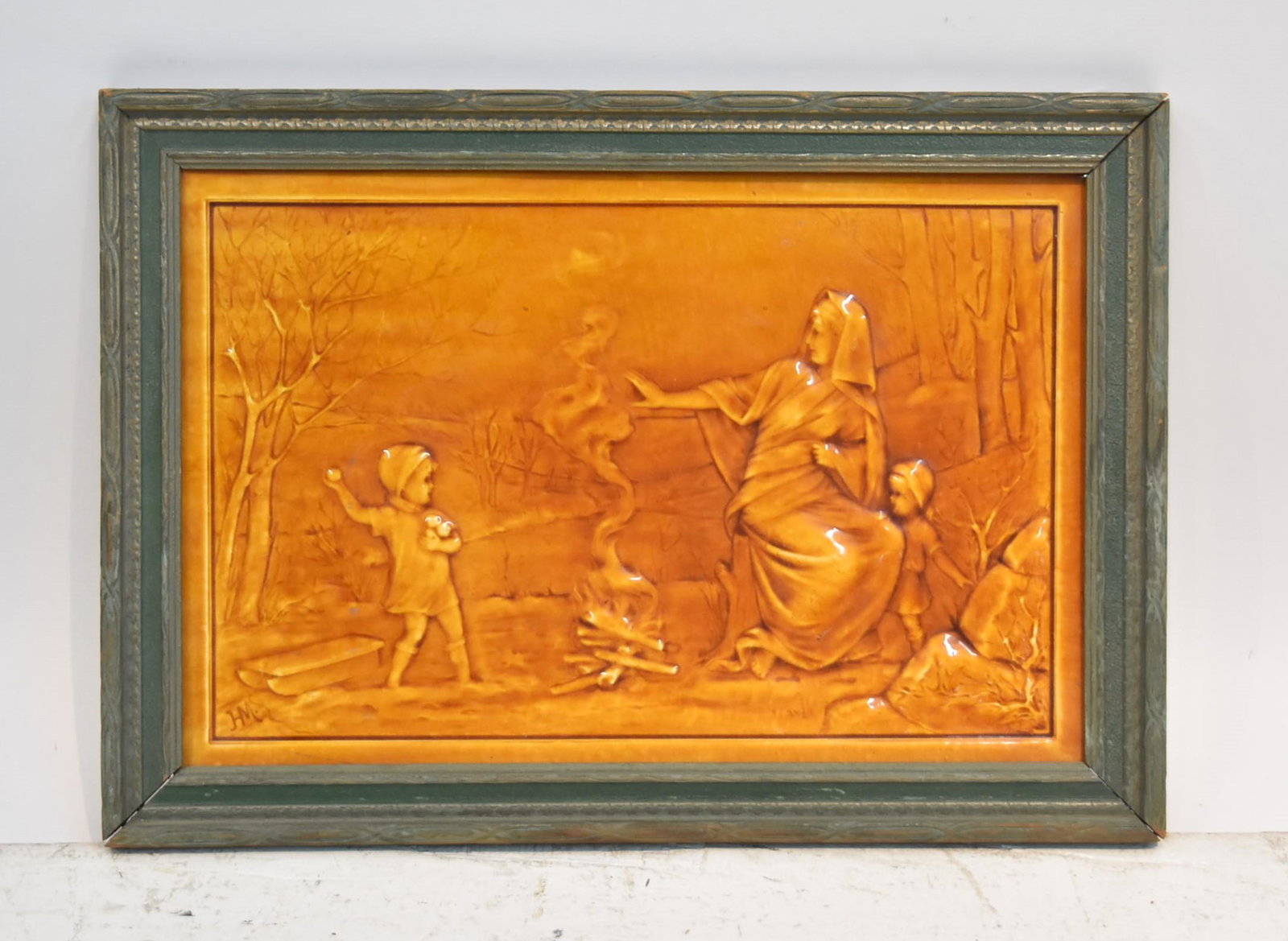 AMERICAN ENCAUSTIC TILE COMPANY CERAMIC PLAQUE: OF WOMAN WITH CHILDREN AROUND CAMPFIRE , ARTIST SIGNED - PLAQUE IS 18" x 11 1/2" ; 21" x 14 1/2" FRAMED