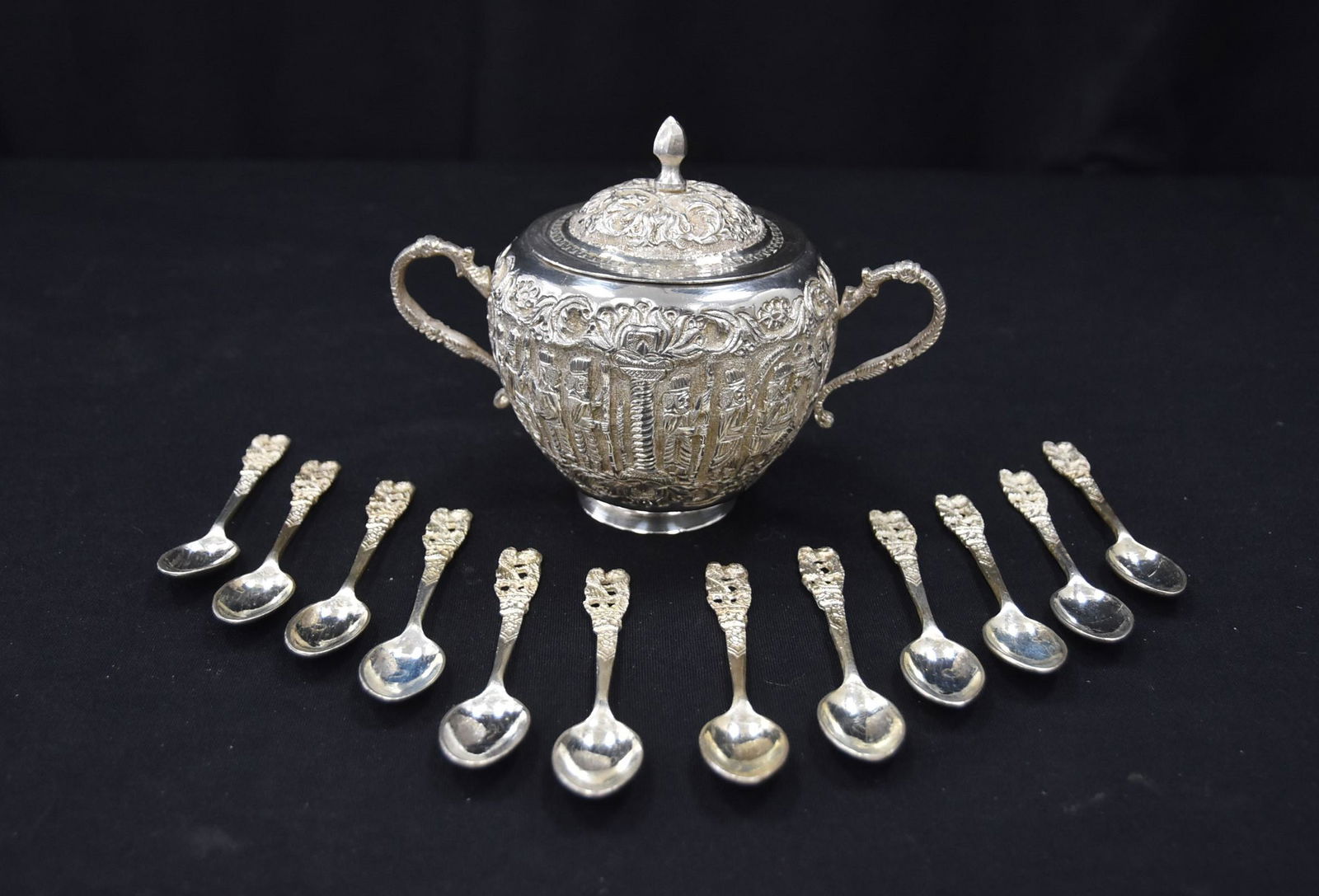 PERSIAN SILVER COVERED SUGAR & SPOONS: RAISED RELEIF PERSIAN SILVER TWIN HANDLE SUGAR WITH FIGURES OF PERSEPOLIS - 6 1/2" x 4" x 5" WITH (12) MATCHING SPOONS - 339.2grams PLUS 186.6grams FOR SPOONS