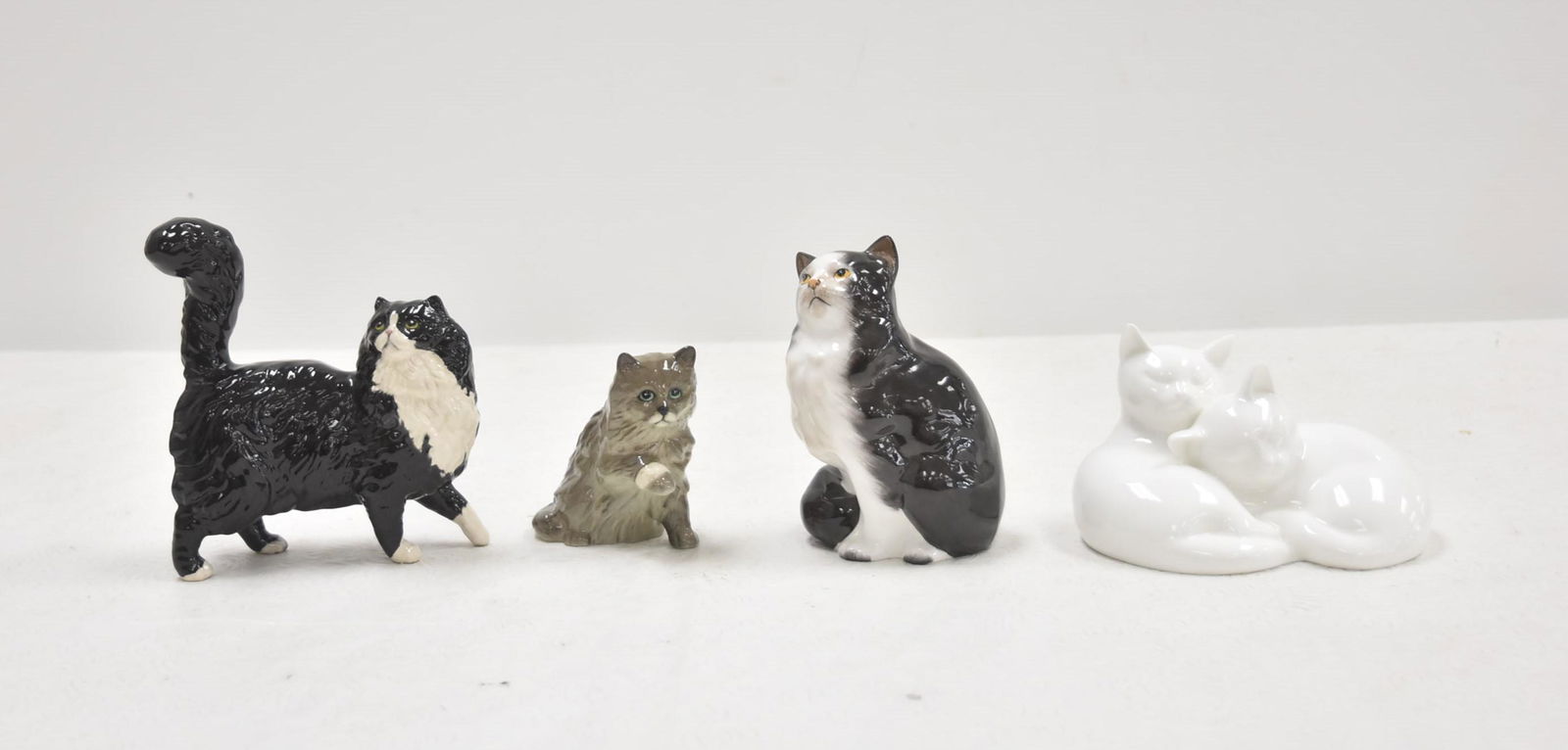 (4) ROYAL DOULTON PORCELAIN CAT MODELS: ROYAL DOULTON CAT WITH BANDAGED PAW , DA 195 / ROYAL DOULTON BLACK & WHITE SEATED PERSIAN CAT ,HN 999 / ROYAL DOULTON PAIR OF CATS "SLEEPY HEADS" HN 3894 / ROYAL DOULTON BLACK & WHITE PERSIAN - TALLES