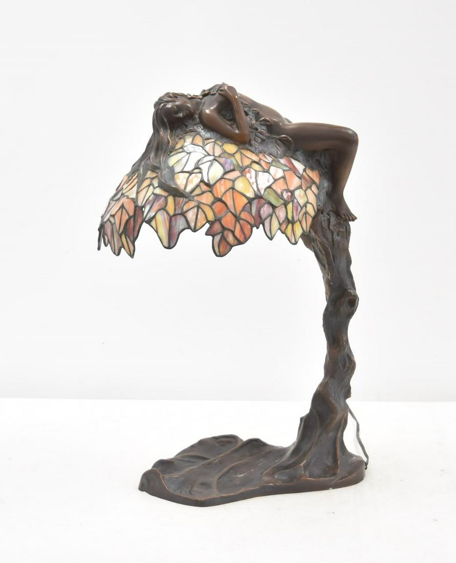 AFTER EMIL THOMASSON BRONZE STAINED GLASS LAMP: AFTER EMIL THOMASSON , BRONZE TREE FROM LAMP WITH BRONZE RECLINING NUDE WOMAN LAYING ON TOP OF FLORAL STAINED GLASS SHADE , SIGNED E THOMASSON - 13" x 8" x 23" (there is one panel that has a line othe