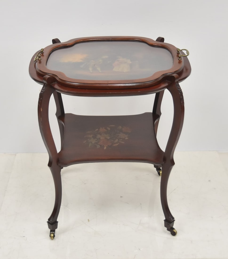 DECORATIVE TRAY TABLE: DECORATIVE TRAY TABLE WITH PAINTED ROMANTIC SCENE UNDER GLASS HANDLED TRAY ; RAISED ON WHEELS - 24" x 27"