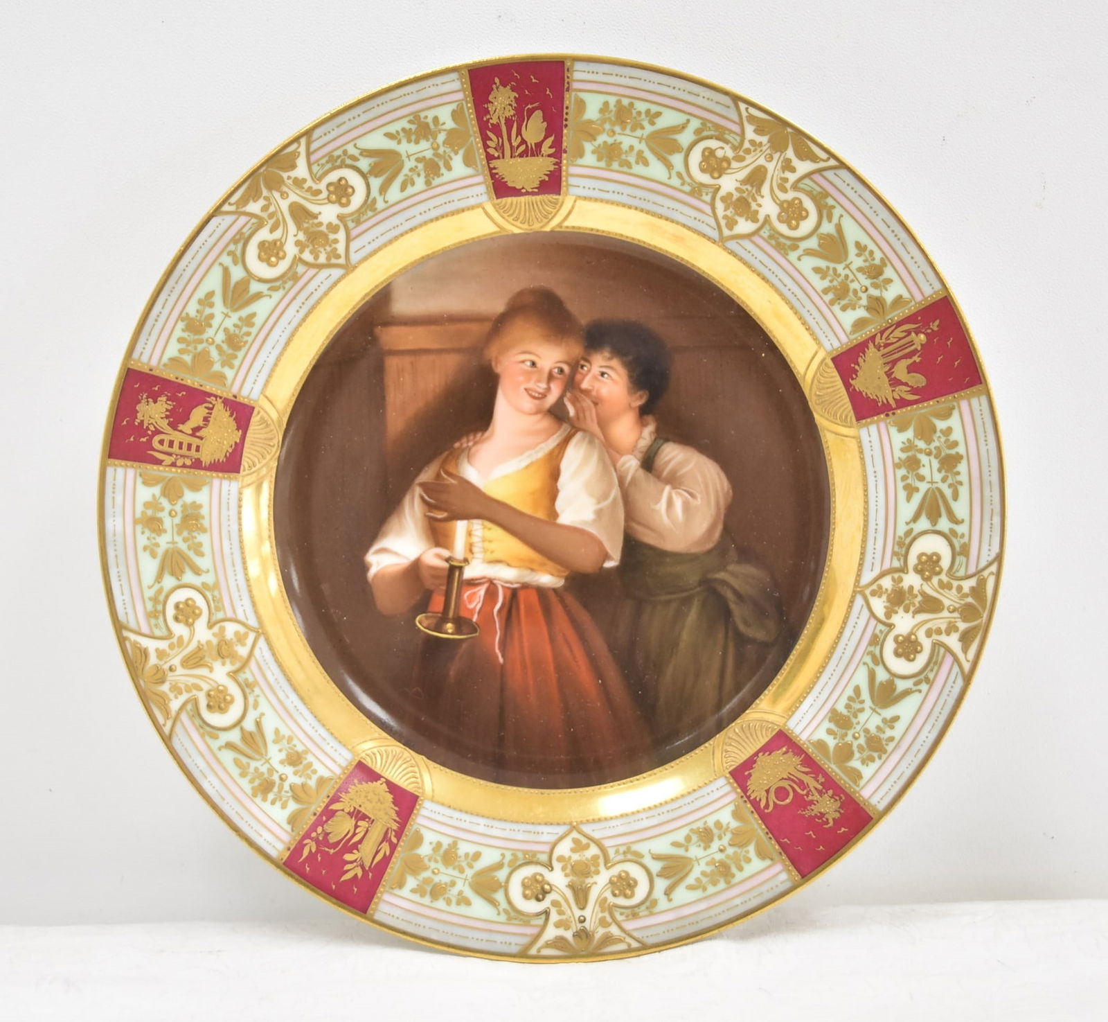 HAND PAINTED ROYAL VIENNA CABINET PLATE: HAND PAINTED ROYAL VIENNA PLATE WITH MAN & WOMAN HOLDING CHAMBERSTICK , TITLED "EIN GEHEIMNISS" , TRANSLATED "A SECRET" ARTIST SIGNED , SURROUNDED BY MULTI COLOR BORDER WITH GOLD DECORATIONS - 9 1/2"