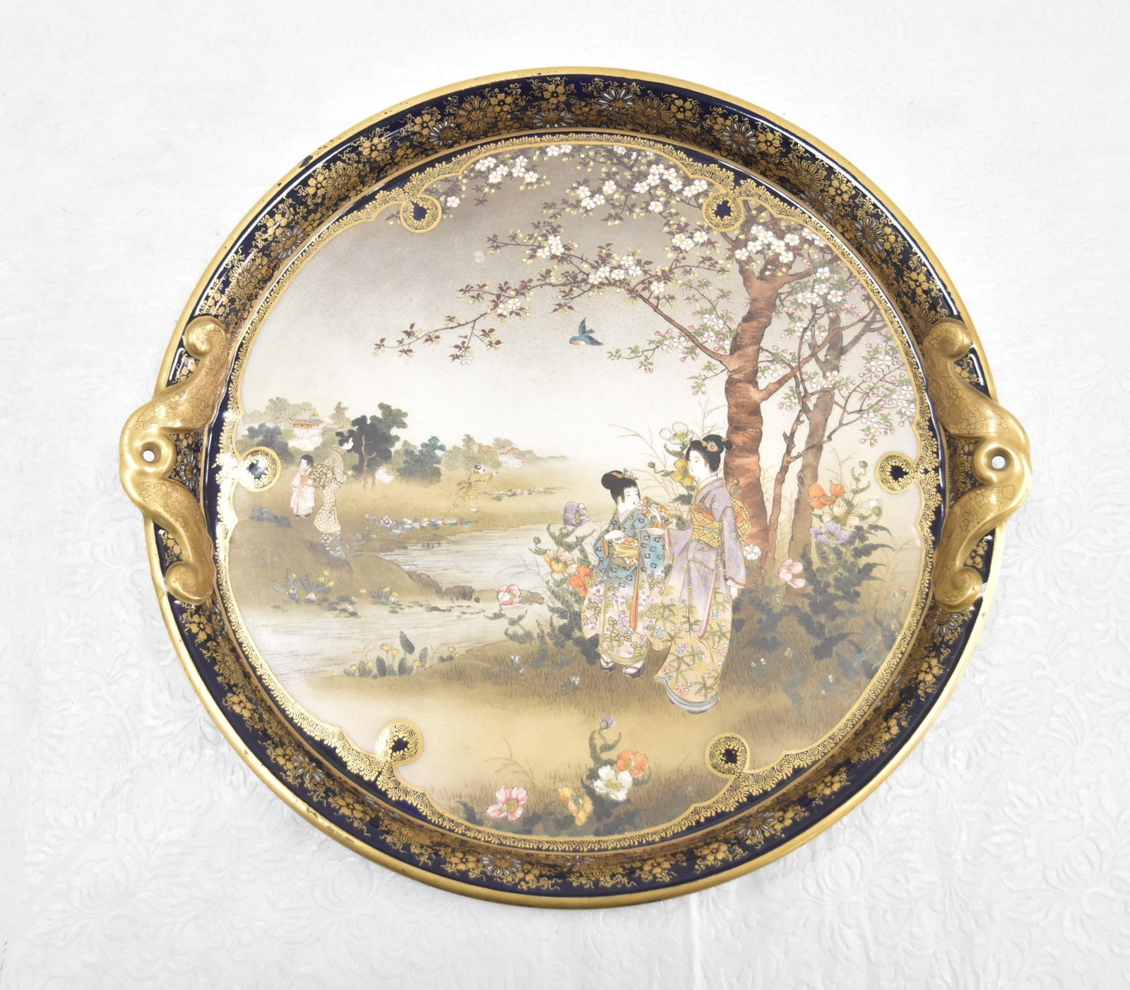 FINE KINKOZAN SATSUMA TRAY: KINKOZAN SATSUMA CHARGER - TRAY WITH ENAMEL GOLD DECORATIONS OVER BLUE GROUND WITH HAND PAINTED FIGURAL SCENES IN RIVER LANDSCAPE WITH TREES & BUTTERFLIES - 13" x 12" x 1 3/4"