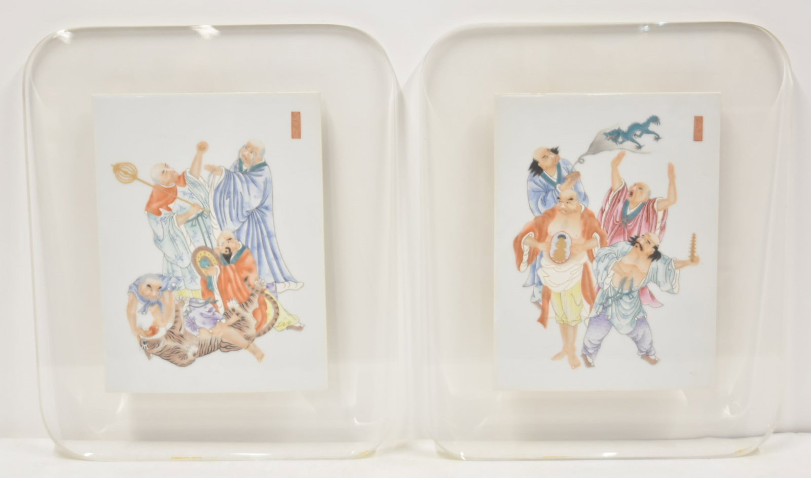 PAIR OF CHINESE PORCELAIN PLAQUES: PAIR OF CHINESE PORCELAIN TILE PLAQUES WITH IMMORTALS CARRYING DRAGON FLAGS & FIGHTING LION , SIGNED , MOUNTED ON LUCITE FRAMES - TILE PLAQUES 9 1/4' x 12 1/2" ; OVERALL IS 15" x 18"