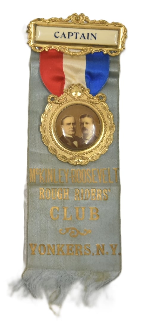 McKINLEY - ROOSEVELT ROUGH RIDERS BADGE: Silk Ribbon attached to celluloid hanger with brass pinback frame and hanging jugate badge supporting the 1900 Republican candidate William McKinley and running mate Theodore Roosevelt. Blue ribbon wi