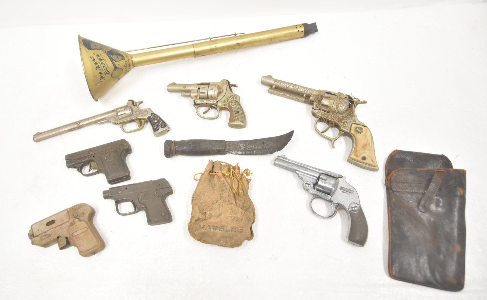 (7) ASSORTED VINTAGE TOY & CAP GUNS: TWO TIME TOY GUN / SURE SHOT TOY GUN / WINNER TOY GUN / HUBLEY POLICE TOY GUN / DANDY TOY GUN / CHAMPION TOY GUN / HOLSTER / RUBBER KNIFE / BOB BURNS SLIDE BAZOOKA INSTRUMENT - 17 1/2" LONG ; LARGEST