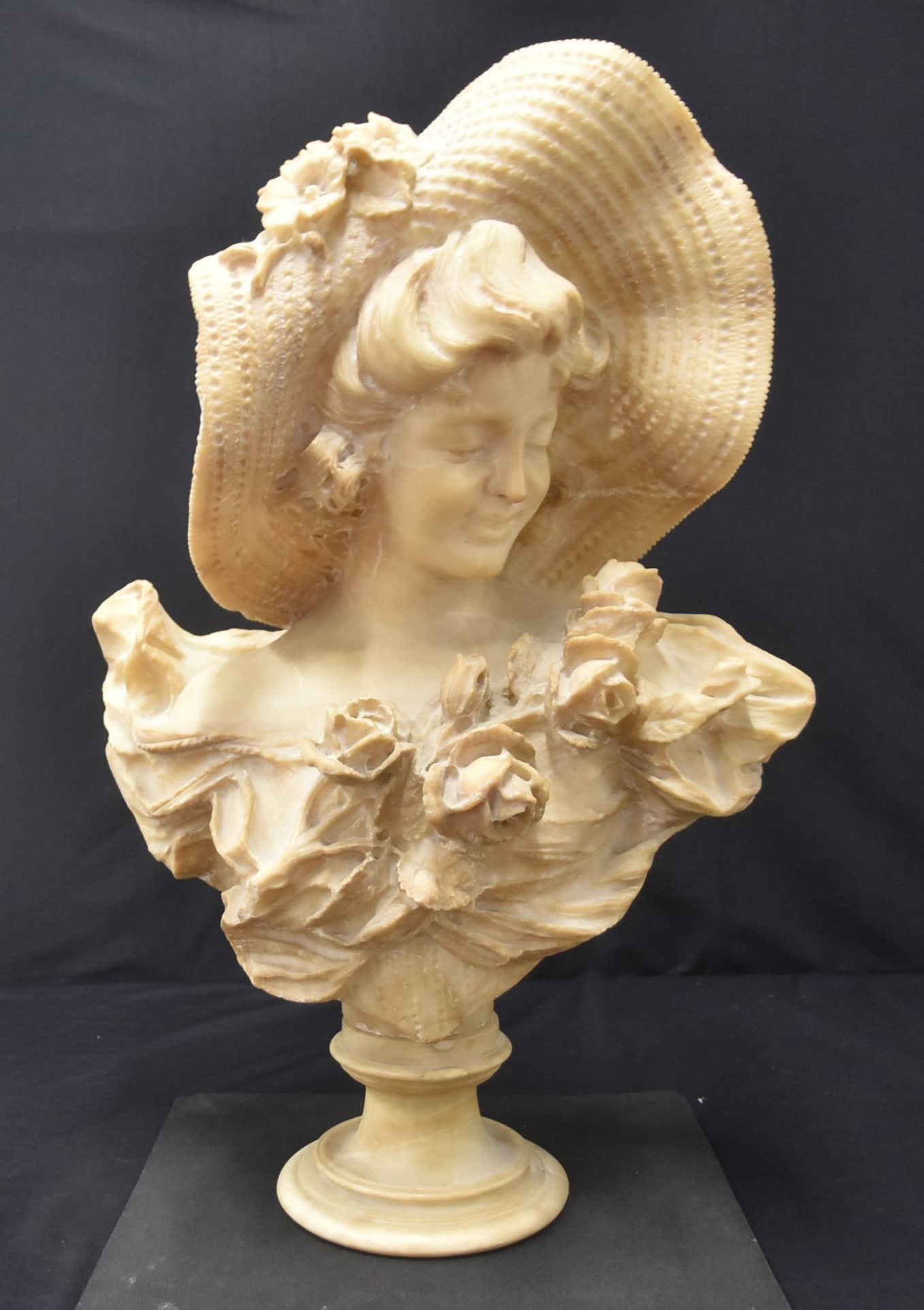 LARGE ALABASTER BUST OF LADY WITH HAT: LARVE CARVED ALABASTER BUST OF LADY WEARING HAT WITH FLOWERS -20" x 10" x 28" Few minor chips on girl & repair on bottom of base