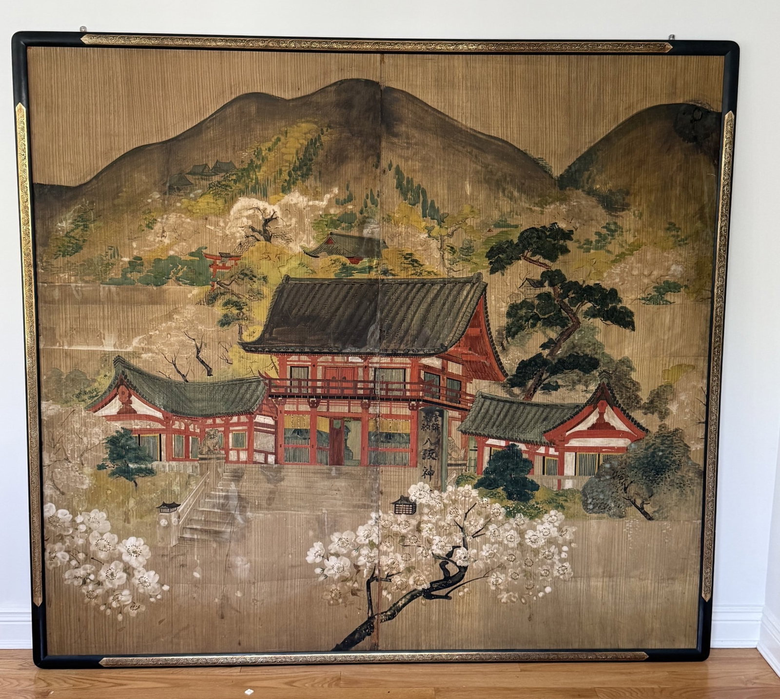 LARGE JAPANESE WOOD PANEL PAINTING: VERY LARGE JAPANESE PAINTING ON WOOD PANEL OF PAGODA HOUSE BY HILLSIDE SURROUNDED WITH CHERRY BLOSSUMS & TRESES ; SIGNED ON DOORWAY - 66" x 74" OVERALL FRAMED (SOME LOSS TO WOOD PANEL) (PLEASE NOTE