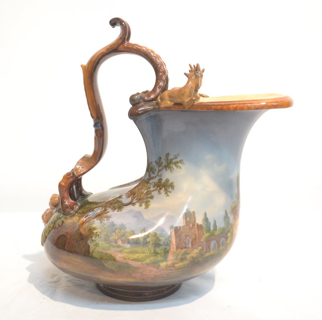 KPM PORCELAIN EWER WITH SCENIC LANDSCAPE: WITH CASTLE AND RUINS HAVING CHERUBS SUPPORTING SCROLL HANDLES & SEATED RAMS SEATED ATOP - 4" x 8" x 9" (MISSING ANTLER)