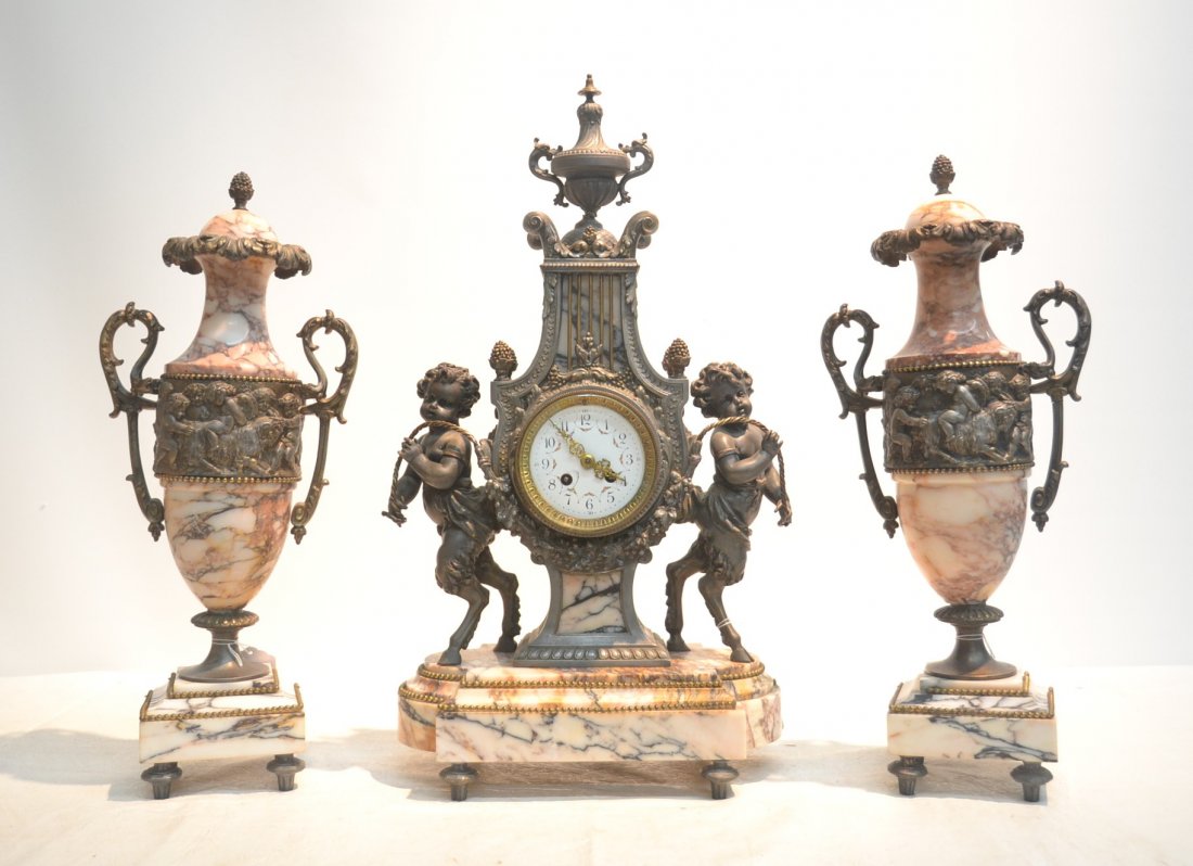 (3)pc DECO WHITE METAL & MARBLE CLOCK SET: WITH PUTTIS ASIDE CLOCK & (Pr) MATCHING GARNITURE WITH PUTTIS & GOATS AROUND ; HAS FRENCH FOUNDRY - CLOCK IS 14" x 7" x 24" , GARNITURE ARE 9" x 21"(URN FINIAL HAS CRACK)