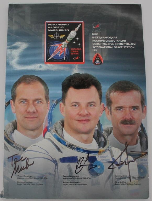 Expedition 35 Crew-Signed Russian Mission Book: An 8"x 11.75" Expedition 35 crew-signed color booklet from Russia and signed on the cover by all three cosmonauts / astronauts with authentic signatures. The booklet contains 120 pages of color photos