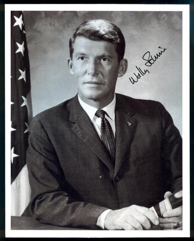 Wally Schirra Signed B&W Glossy Photo: An 8"x 10" B&W glossy paper-like photo signed by Wally Schirra. This looks to be a copy of an original litho, but the signature on it is authentic and not printed. Some handling dings at the top edge